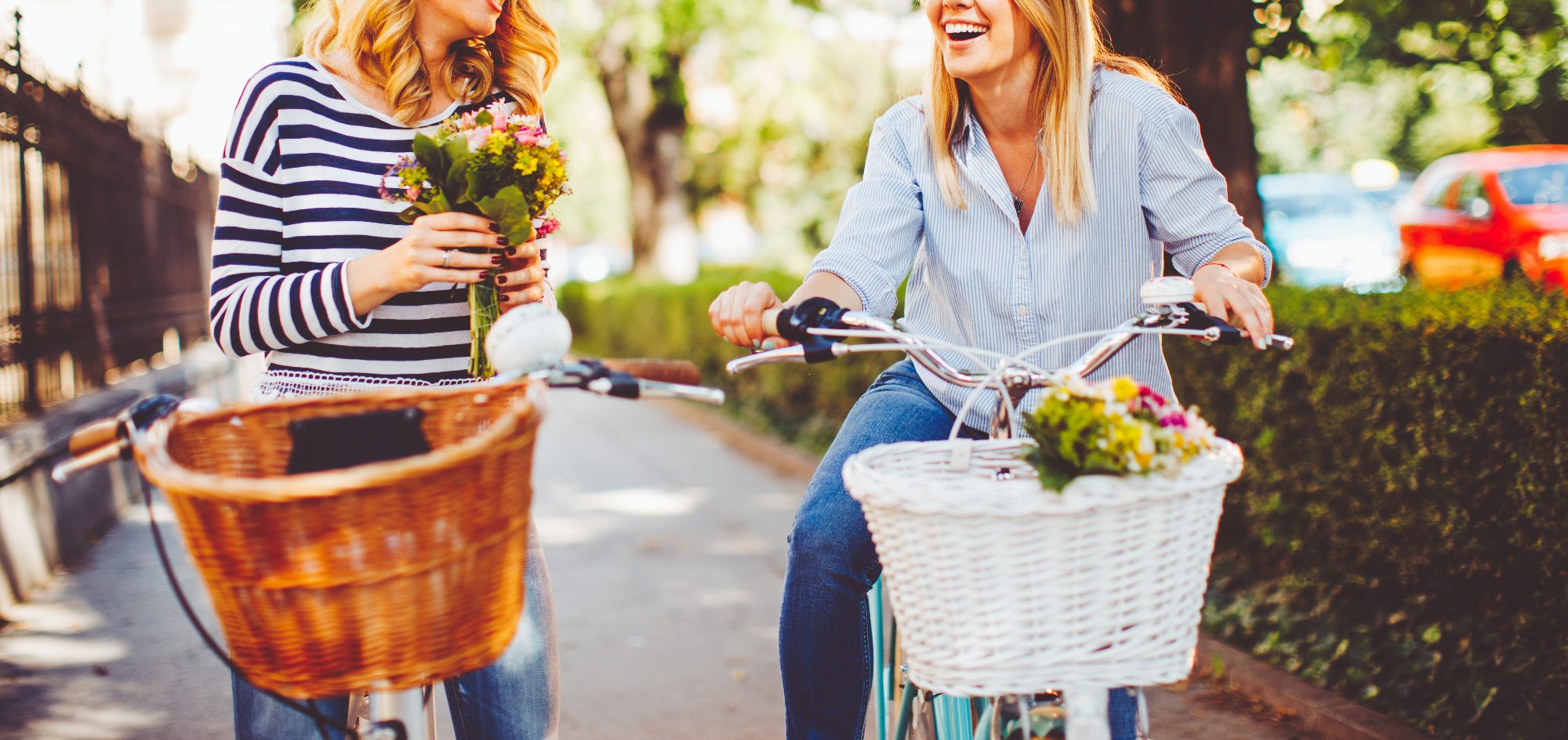 two friends on bikes smiling with flowers in their baskets