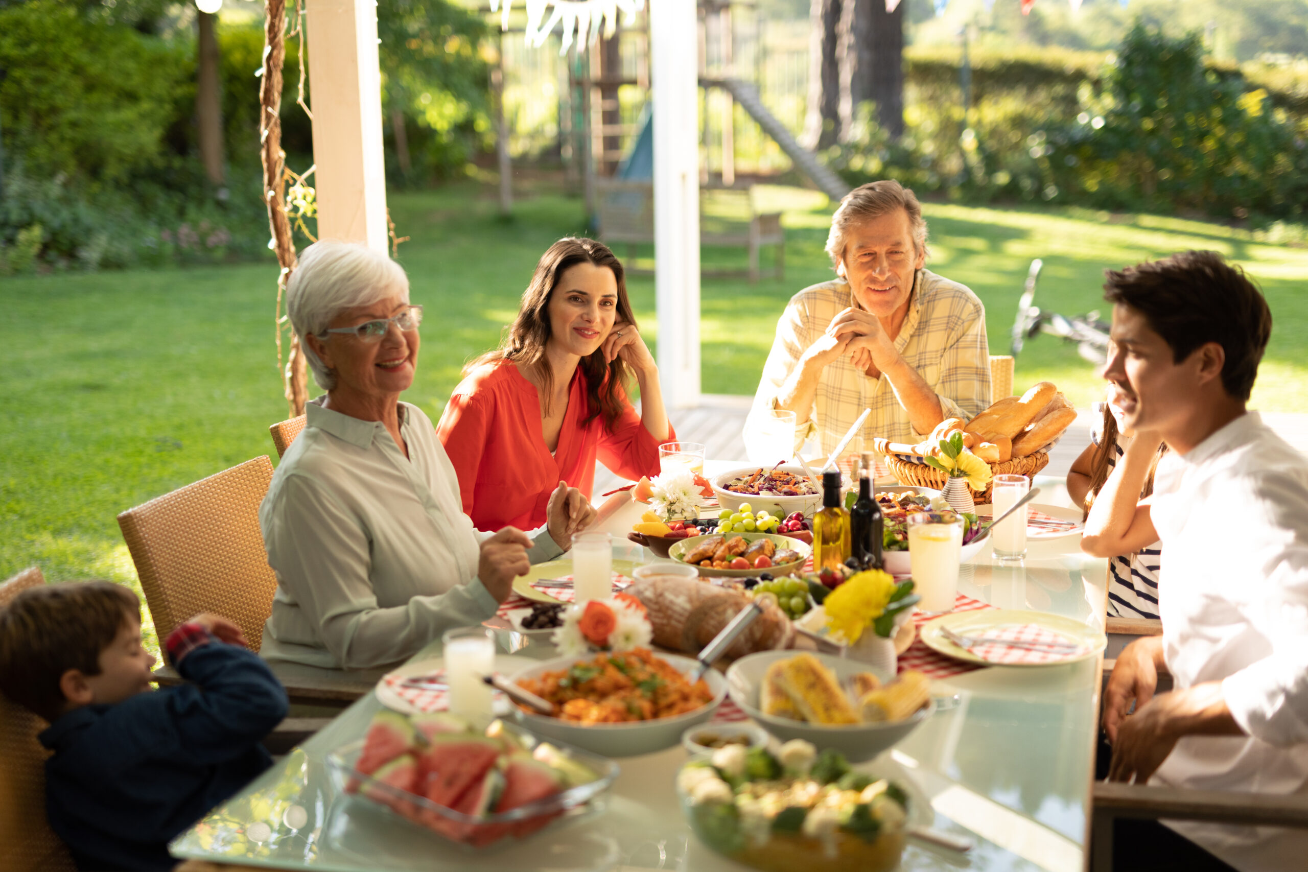 High angle view of a multi-generation Caucasian family sitting outside at a dinner table set for a meal, talking and smiling. Family enjoying time at home, lifestyle concept